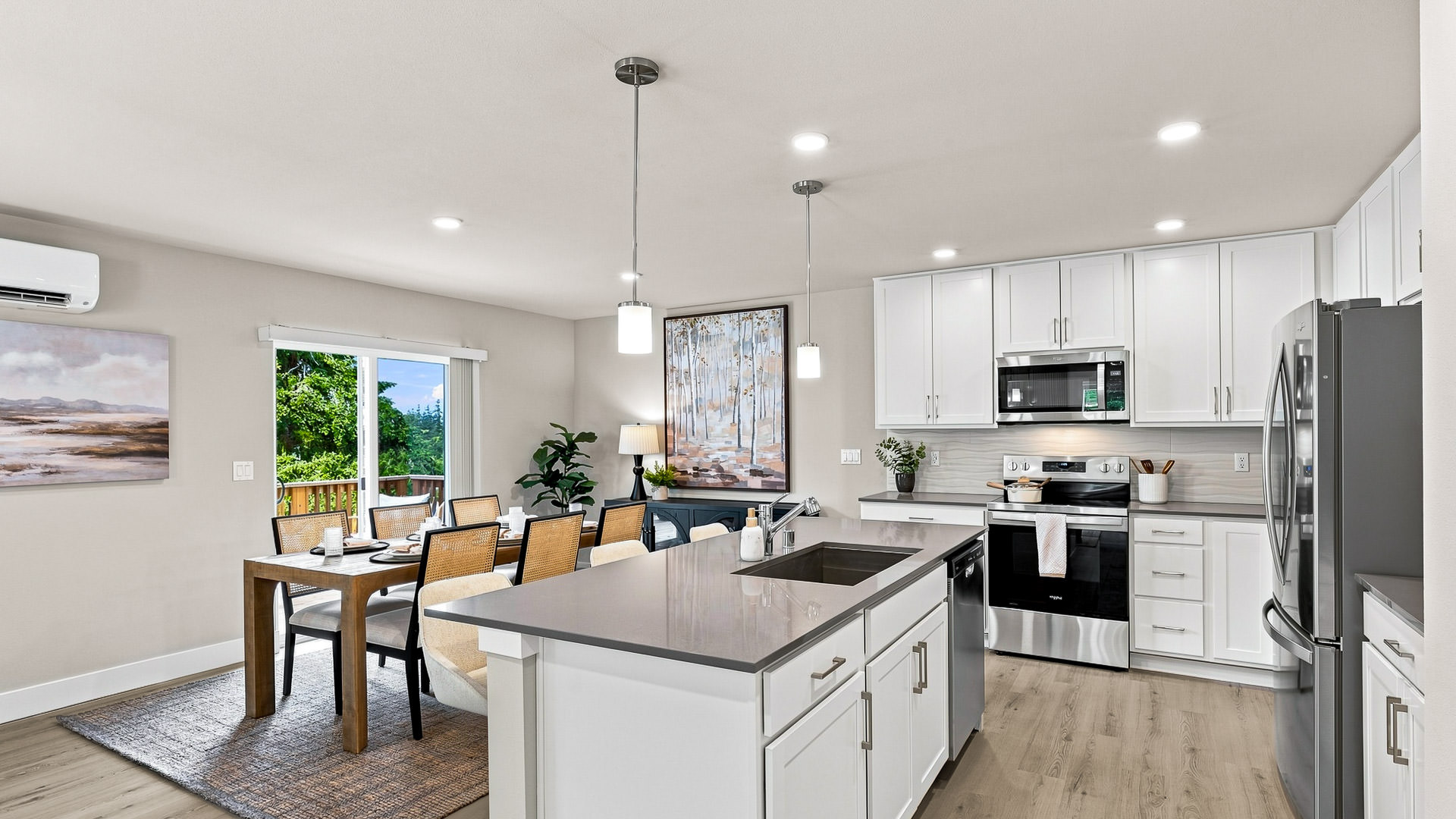 Open kitchen and dining area with a large gray island, white cabinetry, stainless steel appliances, and deck access.
