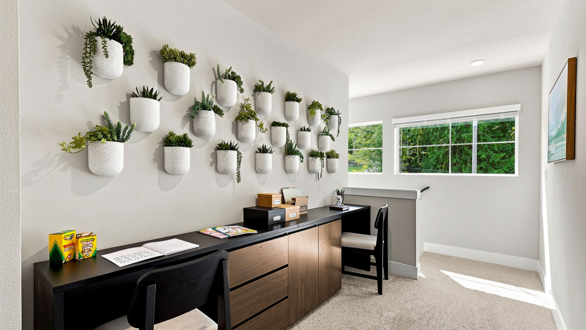 Home office with two workstations, dark wood cabinetry, a wall display of potted plants, and large windows.