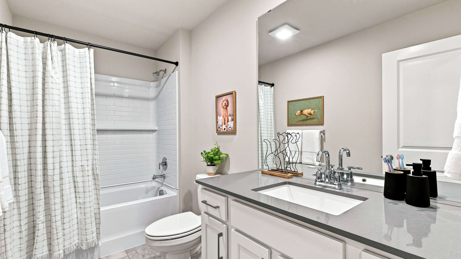 Bathroom with a tub and shower, patterned curtain, white vanity, gray countertop, large mirror, and chrome fixtures.