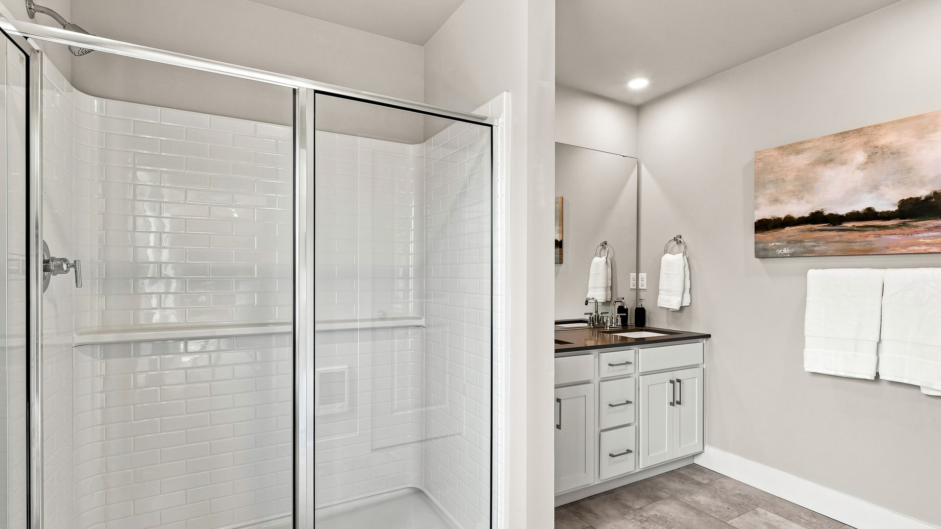 Bathroom with a glass-enclosed subway-tile shower beside a double-sink vanity and wall-mounted towels.