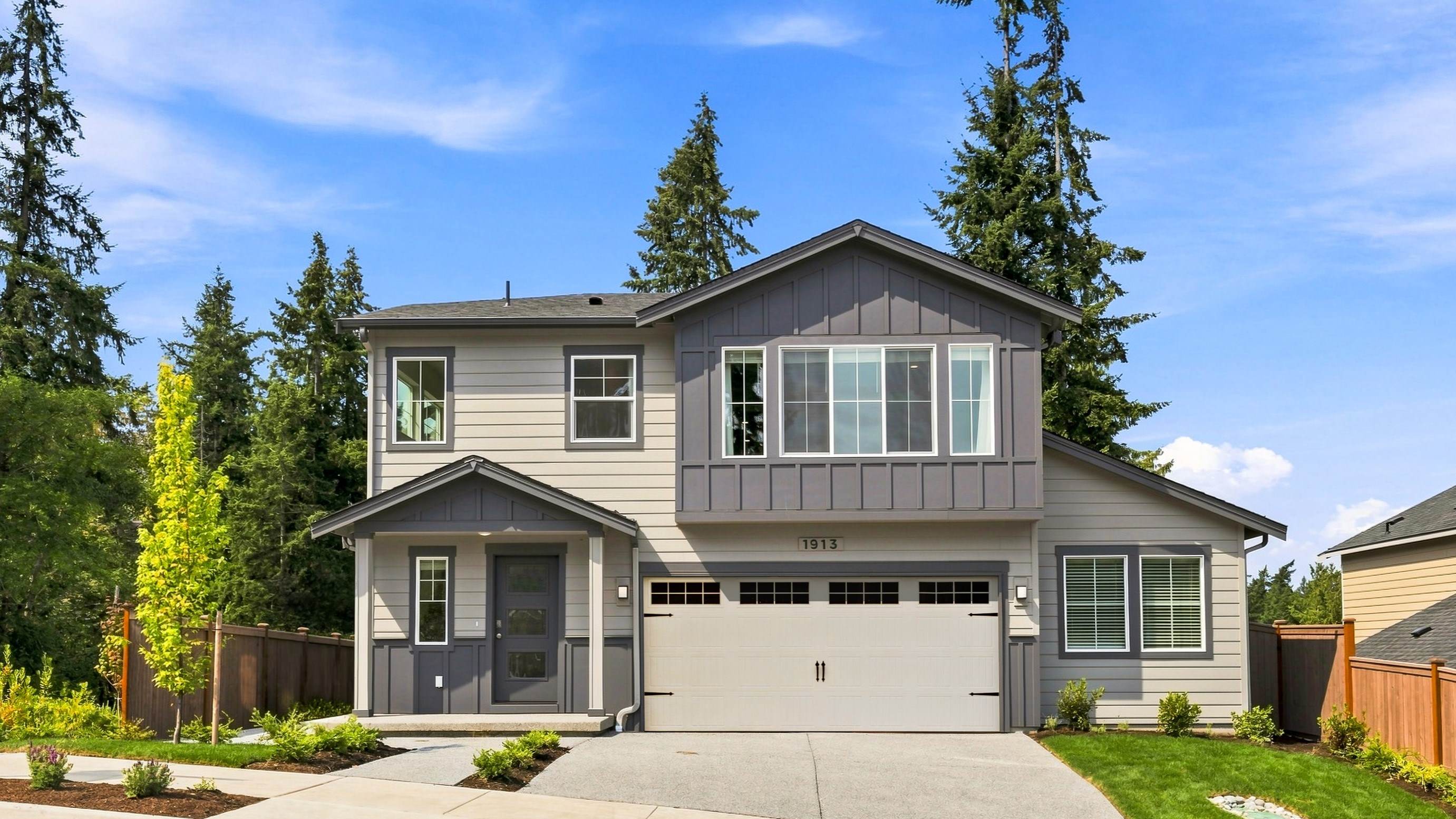 Exterior of the two-story Hudson floor plan with gray siding, dark board-and-batten accents, large windows, covered entry, attached garage, and landscaped front yard.