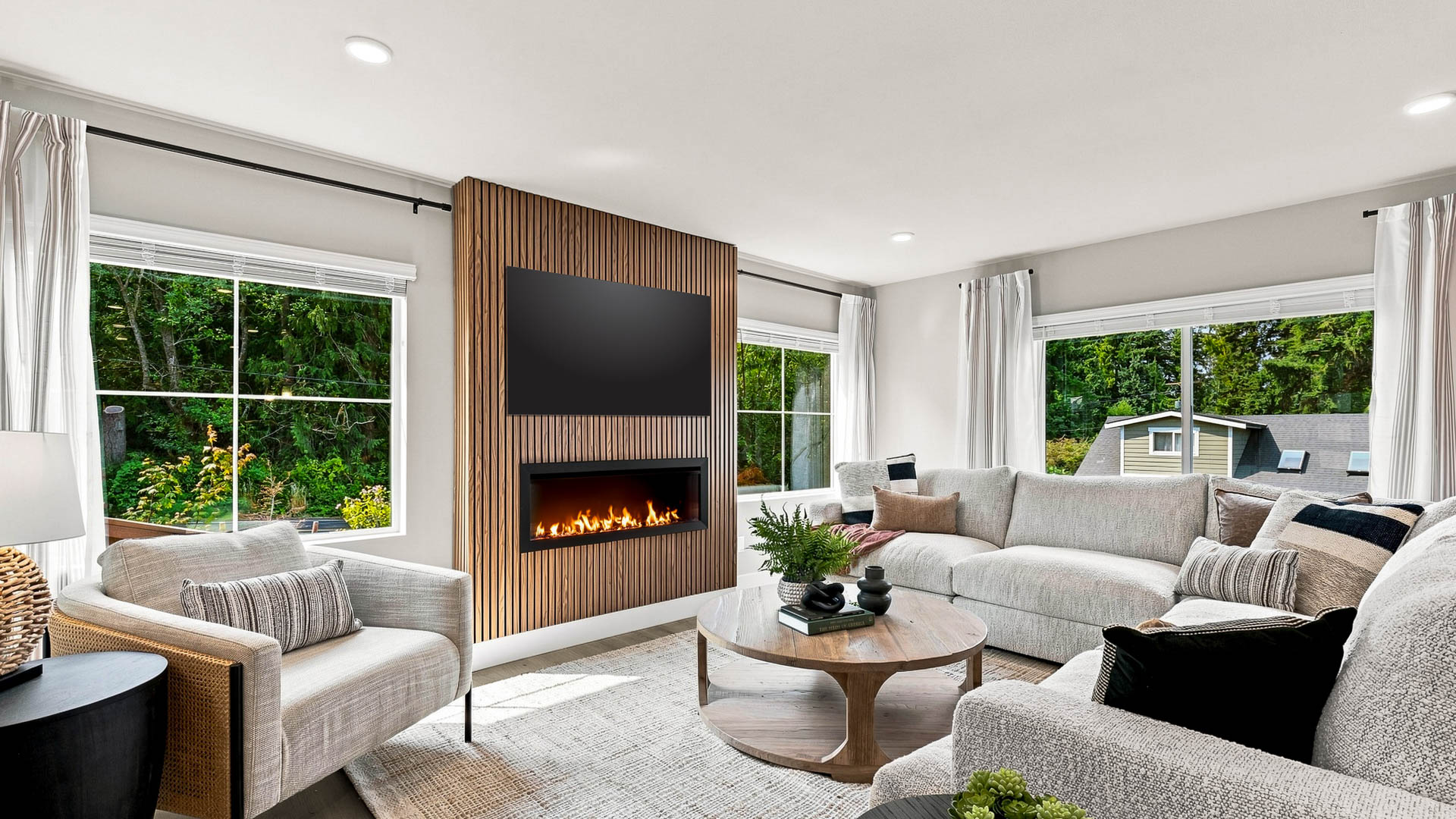 Living room with a sectional sofa, armchair, round wood coffee table, and fireplace beneath a wall-mounted TV.