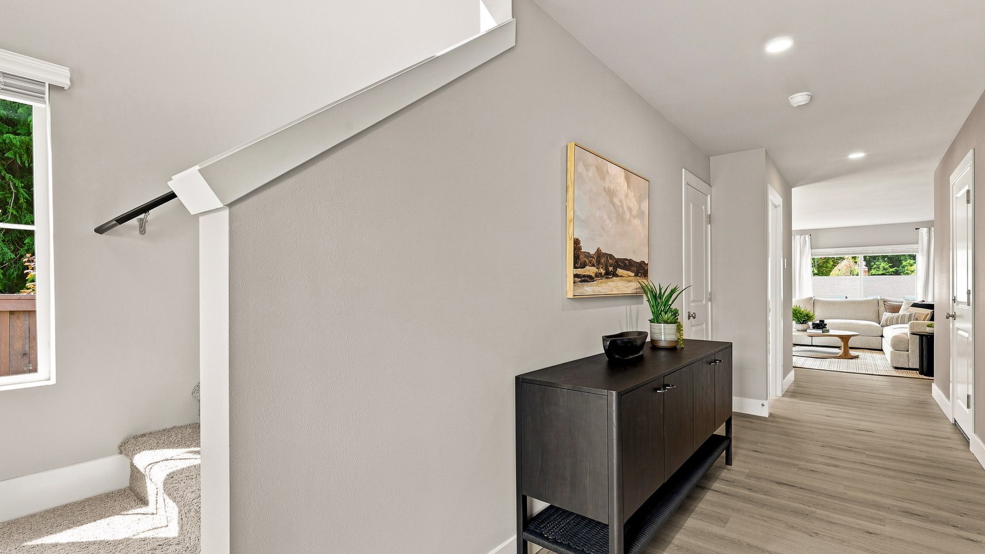 Upstairs hallway with a carpeted staircase, dark wood console, framed artwork, and a view into the living room.