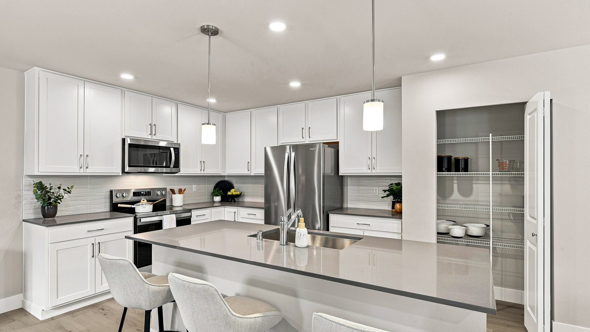 White kitchen with gray countertops, stainless steel appliances, pendant lights, an island sink, and an open pantry.