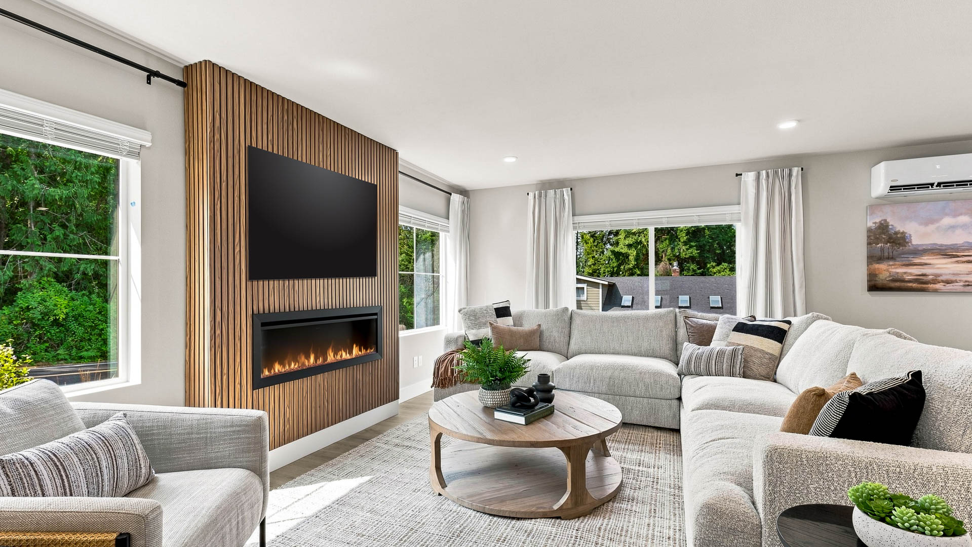 Bright living room with a large sectional sofa, round coffee table, modern fireplace, wood accent wall, and large windows.