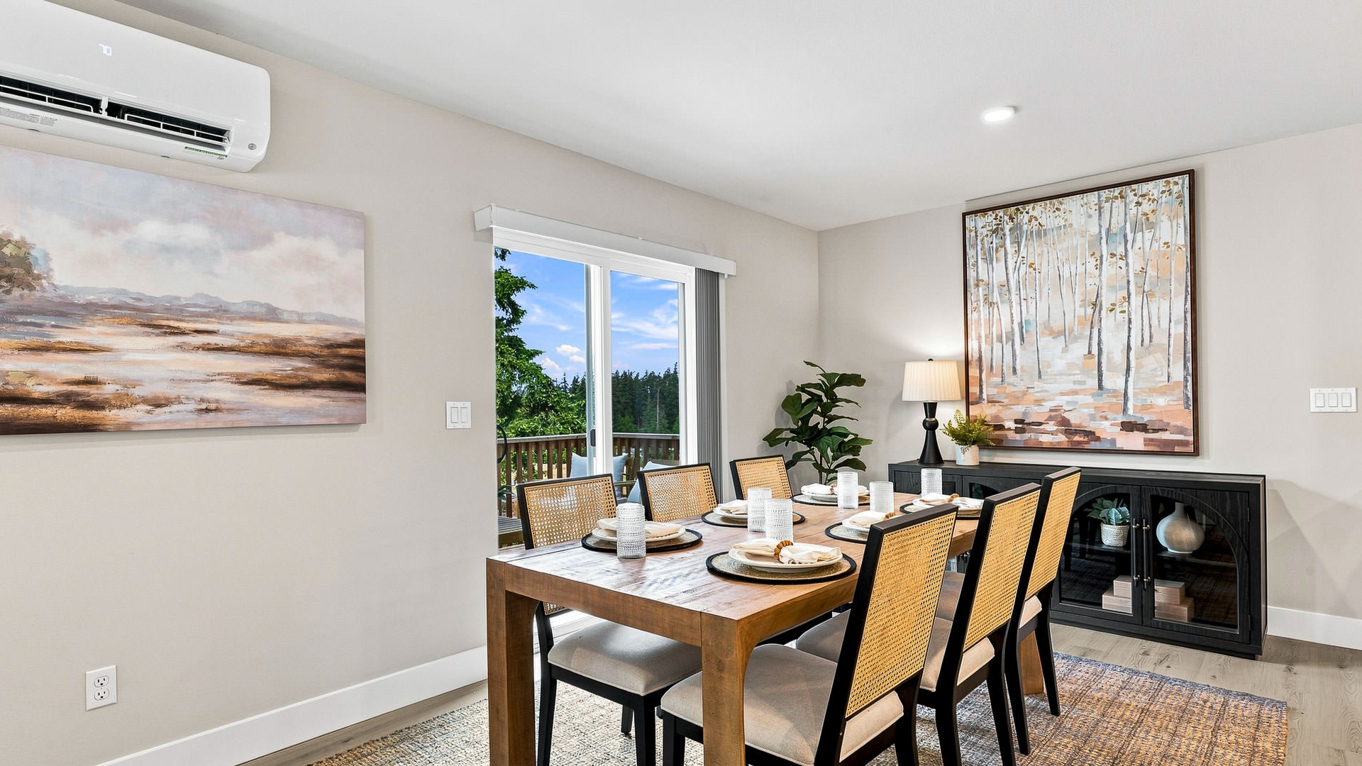 Dining room with a wood table and woven-back chairs, large artwork, sliding glass door, and access to an outdoor deck.