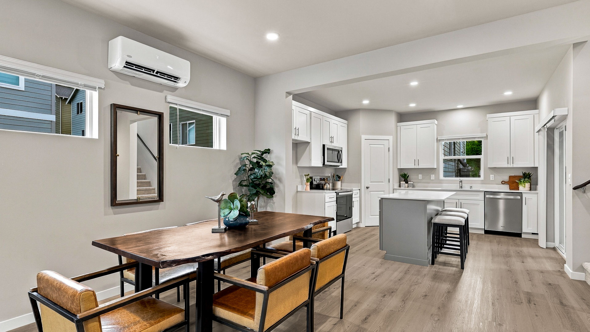 Modern kitchen with white perimeter cabinets, gray island with quartz countertop, stainless steel appliances, wood-look flooring, and sliding doors to a covered balcony.