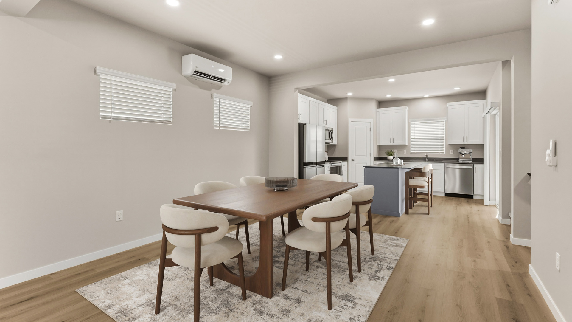 Open dining area with a rectangular wood table, six cream upholstered chairs, an area rug, and the white kitchen in the background.