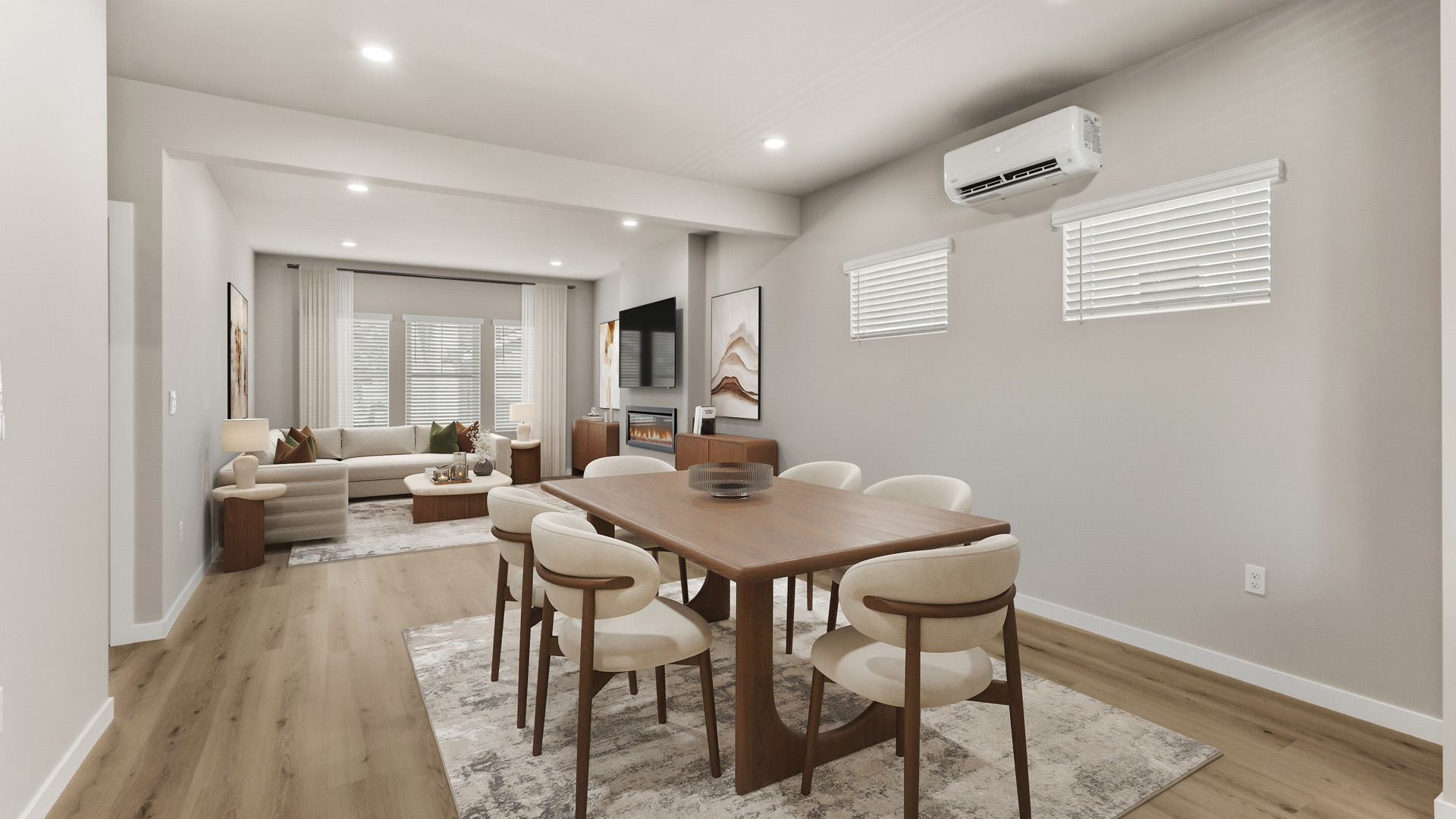 Open-plan dining and living area with a wood table and six cream chairs in the foreground and a sofa, fireplace, and wall-mounted TV beyond.