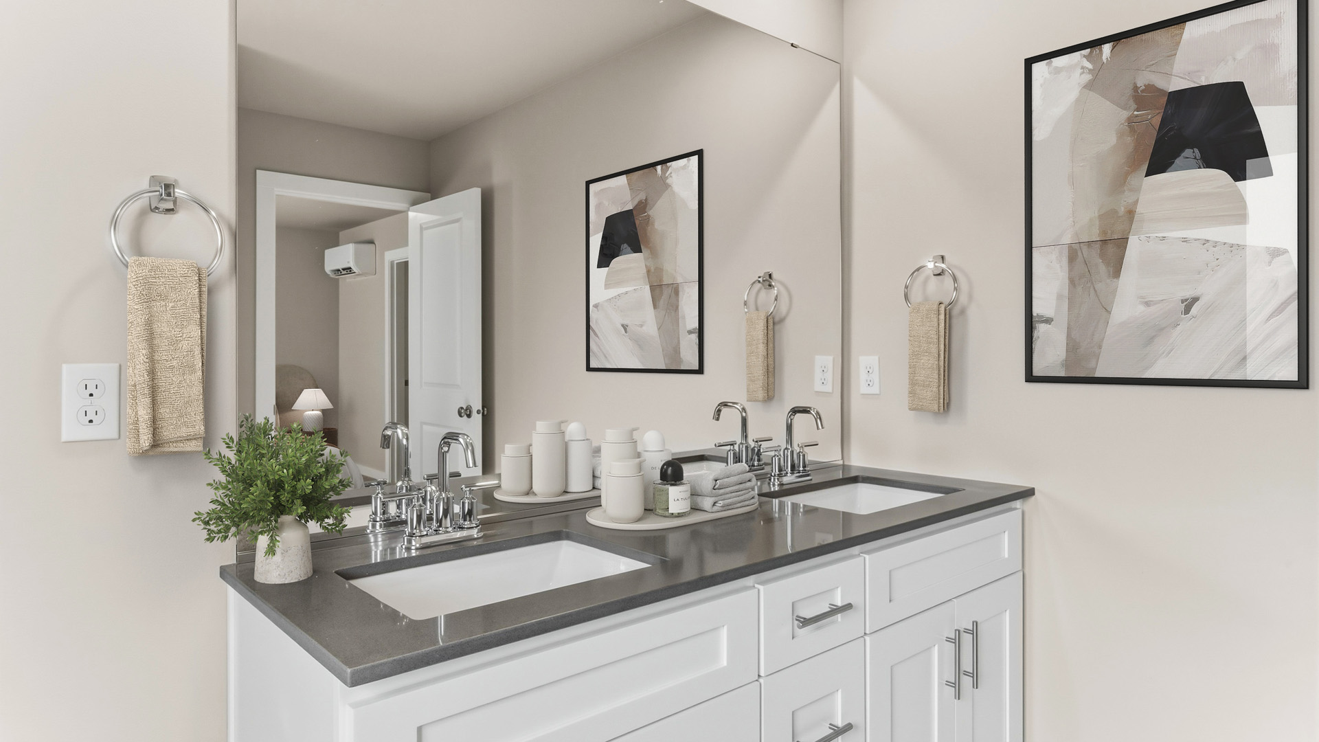 Double bathroom vanity with white cabinets, gray countertop, two rectangular sinks, chrome faucets, a wall-to-wall mirror, hand towels, and abstract artwork.