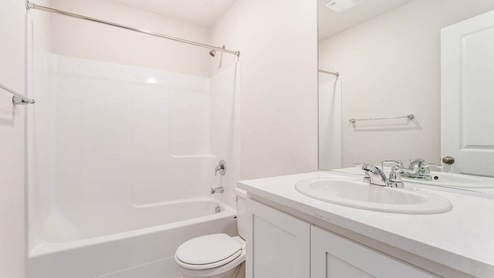 main level bathroom with white cabinet, white toilet, and combination shower / tub