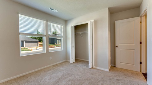 A bedroom with white walls, wall-to-wall carpet, a window and a closet