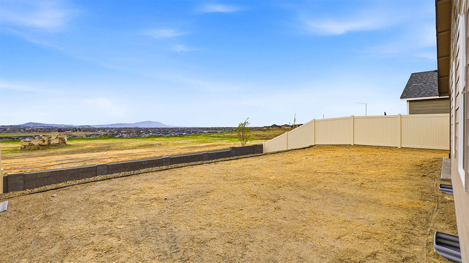 fully fenced backyard with bark chips and a patio