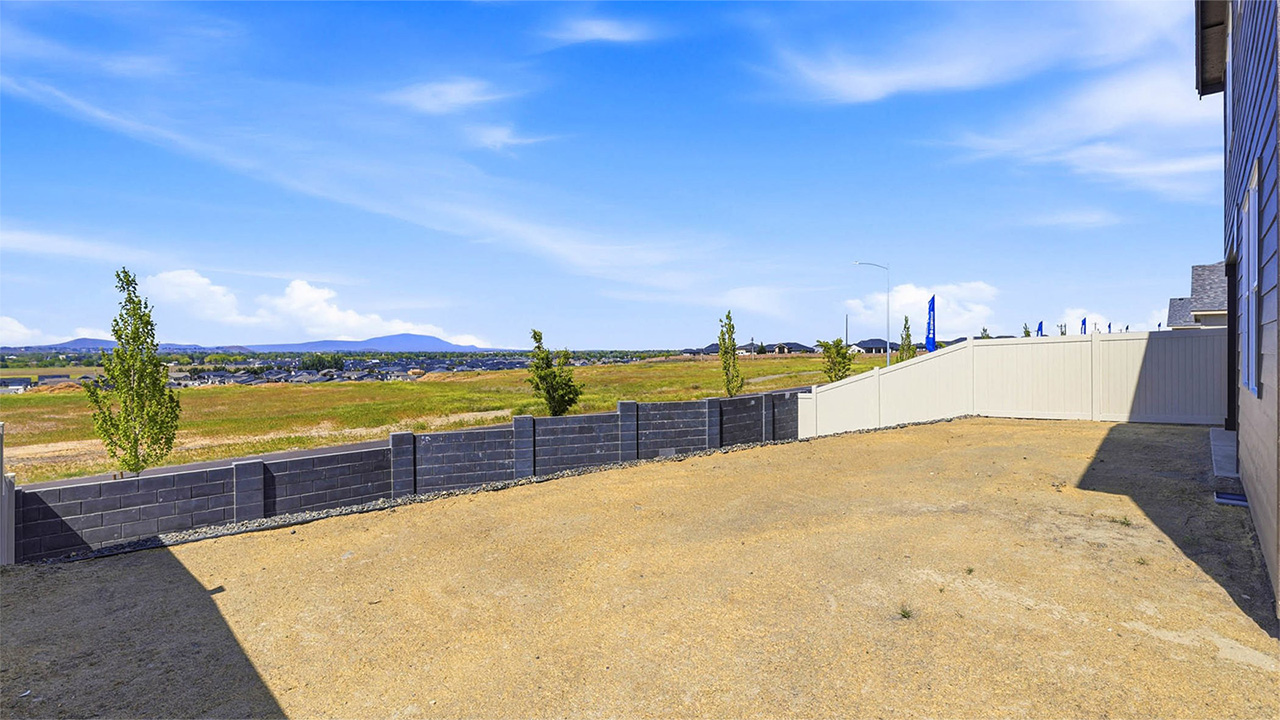 fully fenced backyard with bark chips and a patio