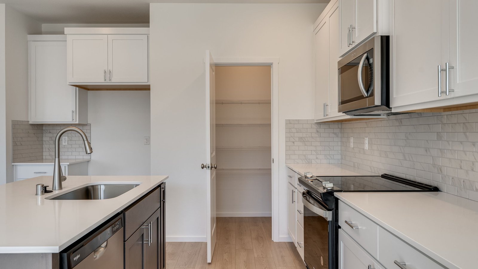 Kitchen with shaker cabinets, quartz counters, stainless steel appliances, pantry, and an island with a breakfast bar