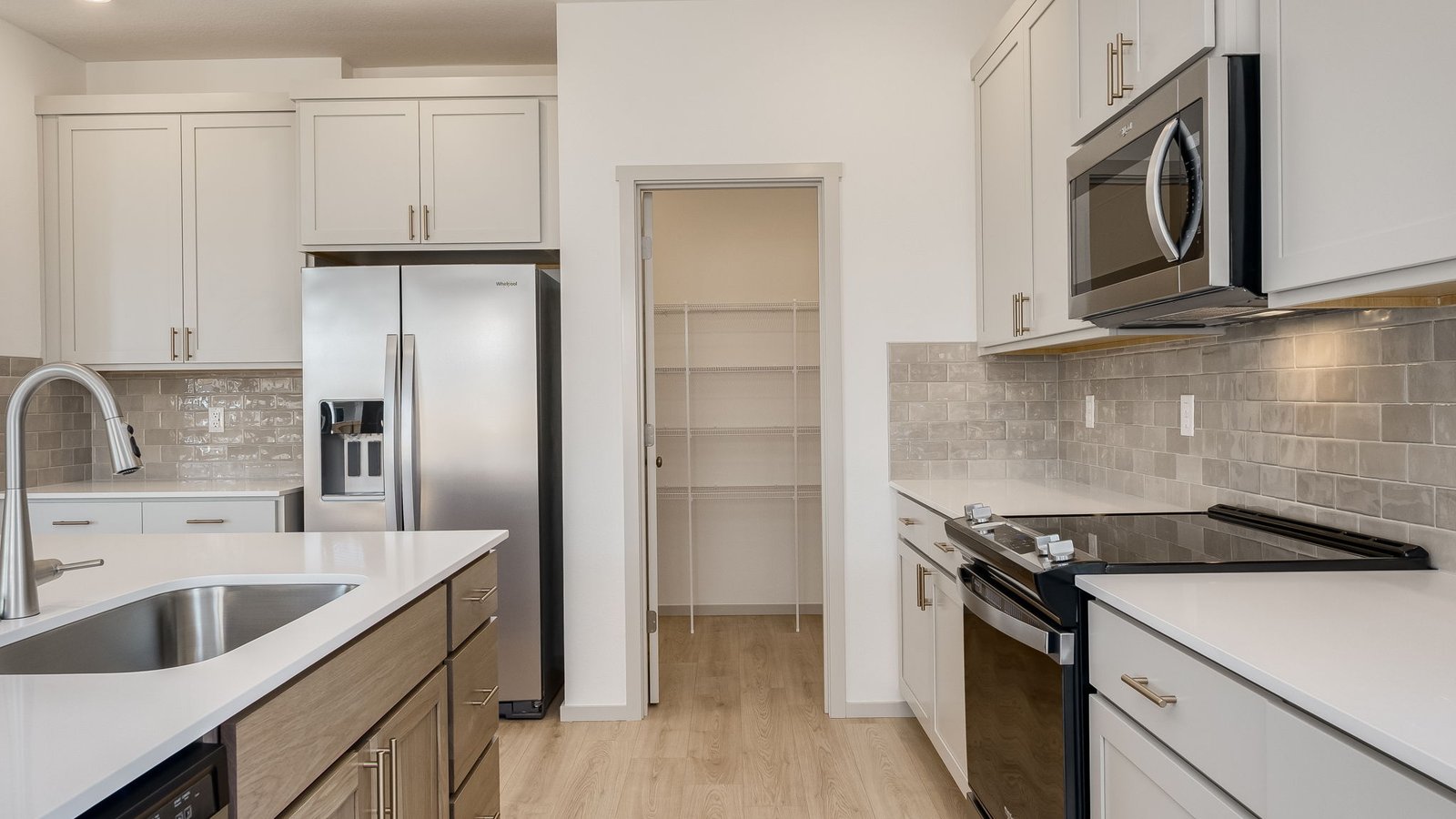 Kitchen with shaker cabinets, quartz counters, stainless steel appliances, pantry, and an island with a breakfast bar