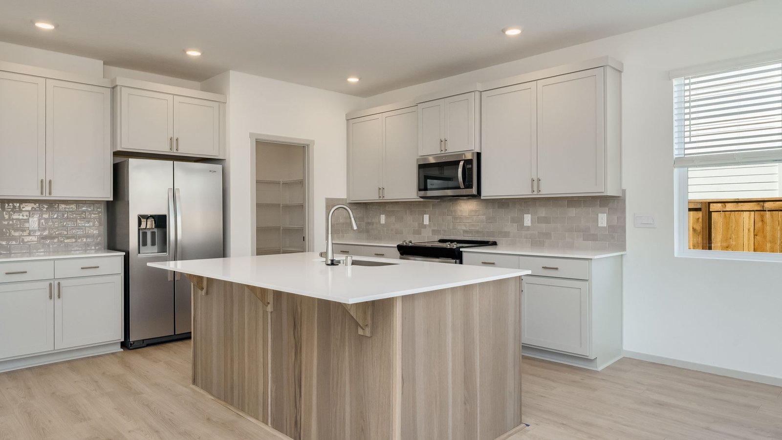 Kitchen with shaker cabinets, quartz counters, stainless steel appliances, pantry, and an island with a breakfast bar