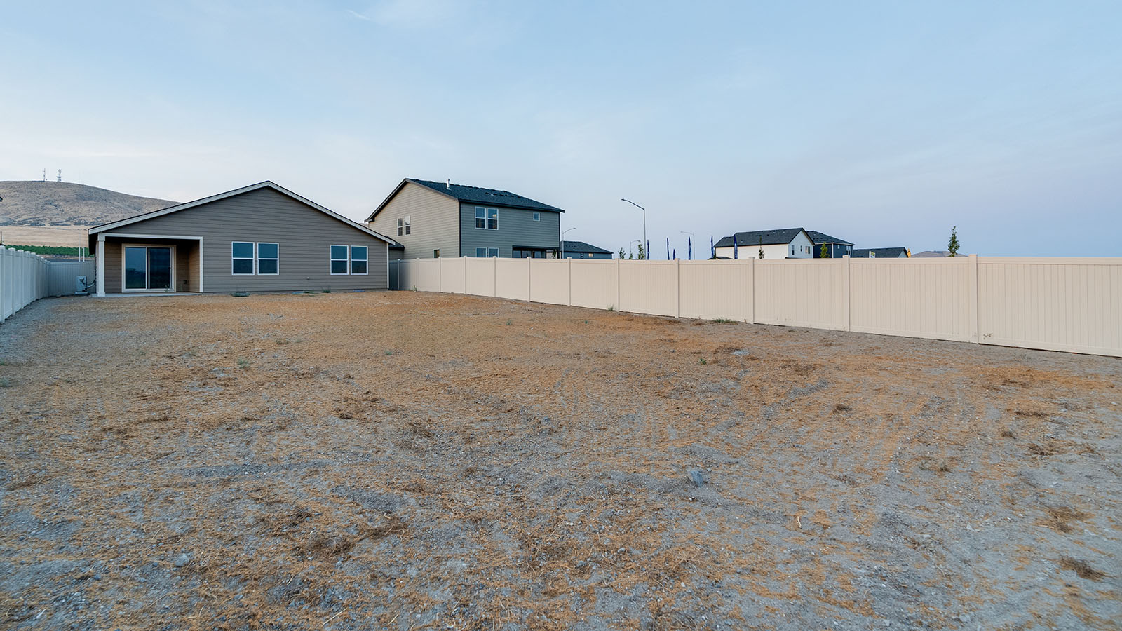fully fenced backyard with bark chips and a patio