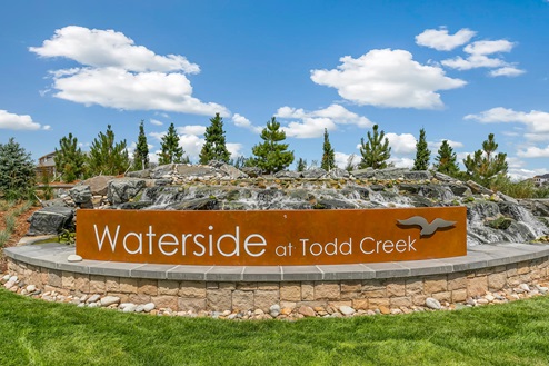 Community monument sign with cascading water feature and treeline in background "Waterside at Todd Creek"