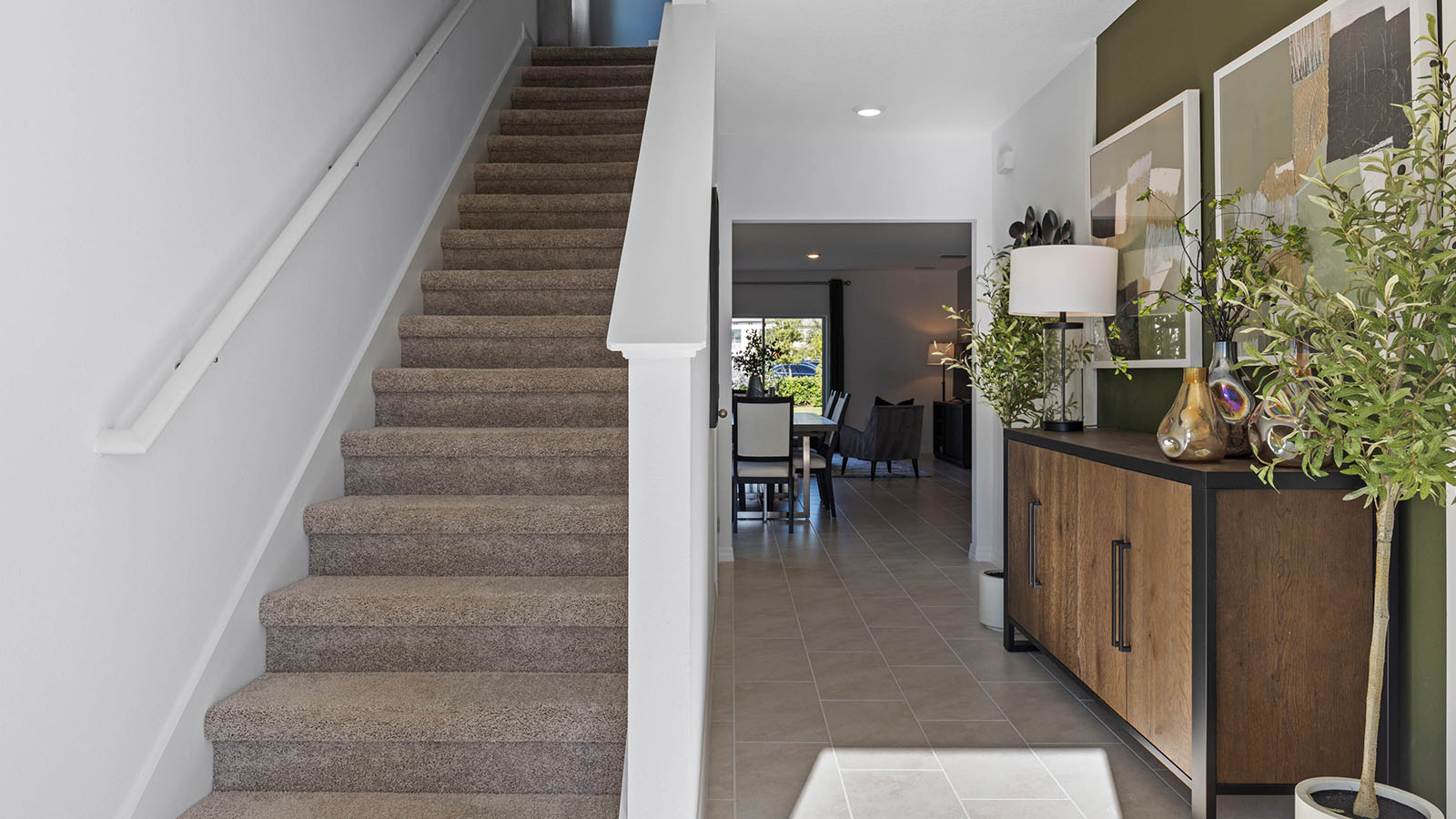 Entryway with stairs to second floor and cabinet with artwork in hallway to main living spaces