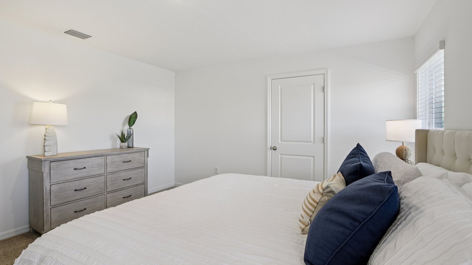 Spacious primary bedroom with king size bed, carpet flooring, natural lighting and a walk in closet.