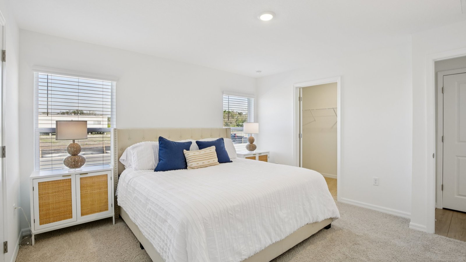 Spacious primary bedroom with king size bed, carpet flooring, natural lighting and a walk in closet.