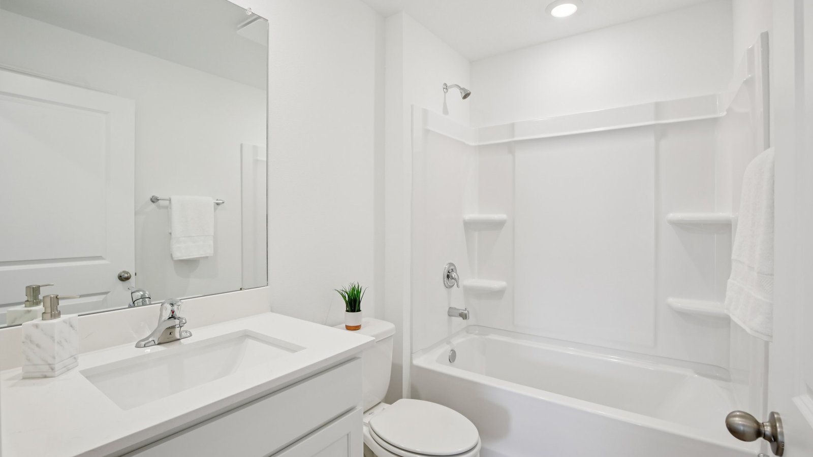 Modern bathroom with single bowl sink, quartz vanity, wall mirror, cabinets and toilet.