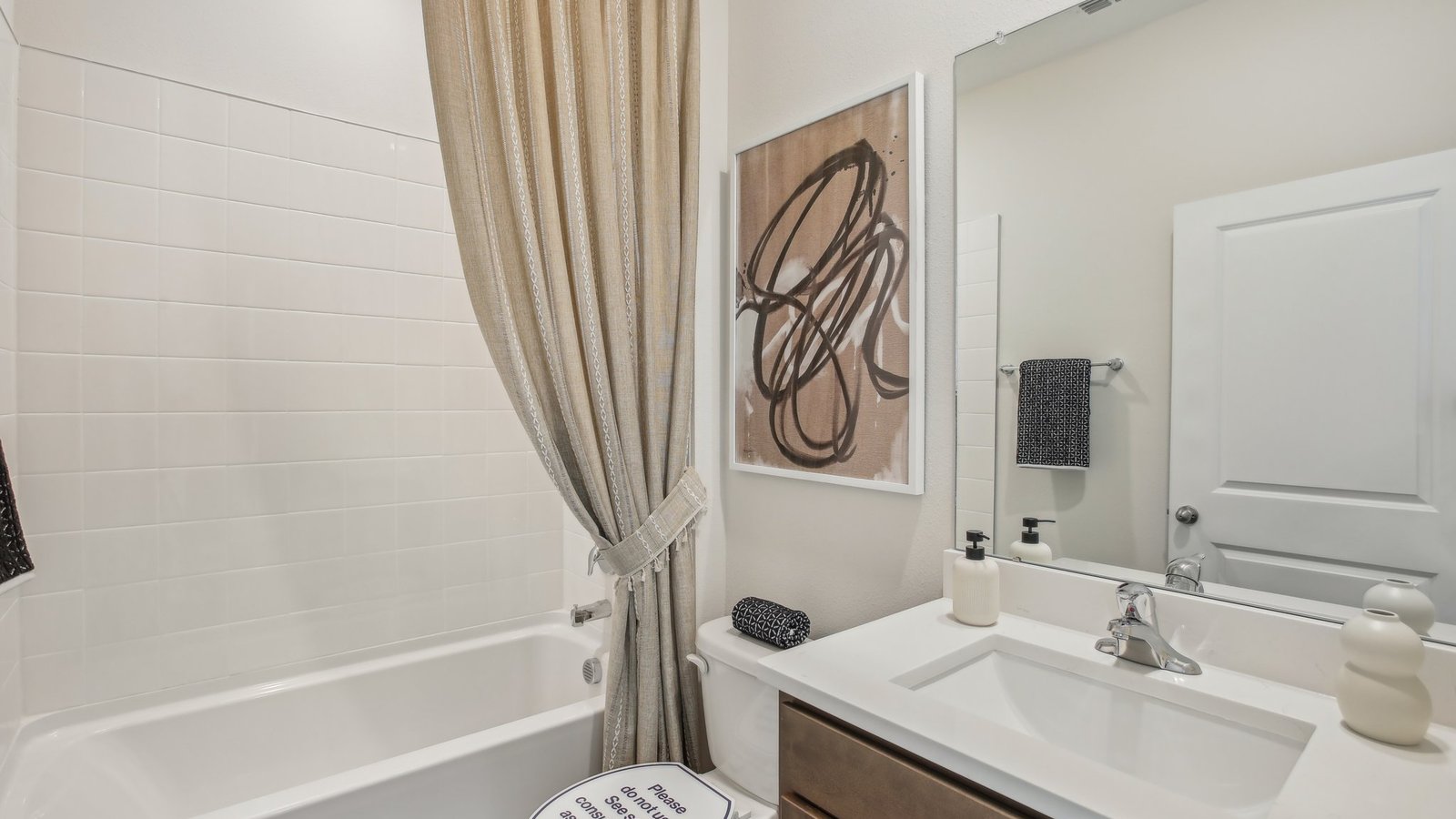 Modern bathroom with single bowl sink, quartz vanity, wall mirror, cabinets and toilet.