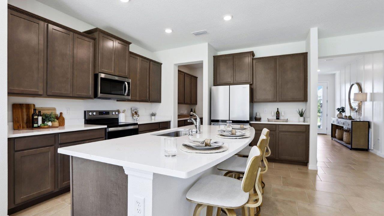 Kitchen with island seating, quartz counters, spacious pantry and stainless-steel appliances.