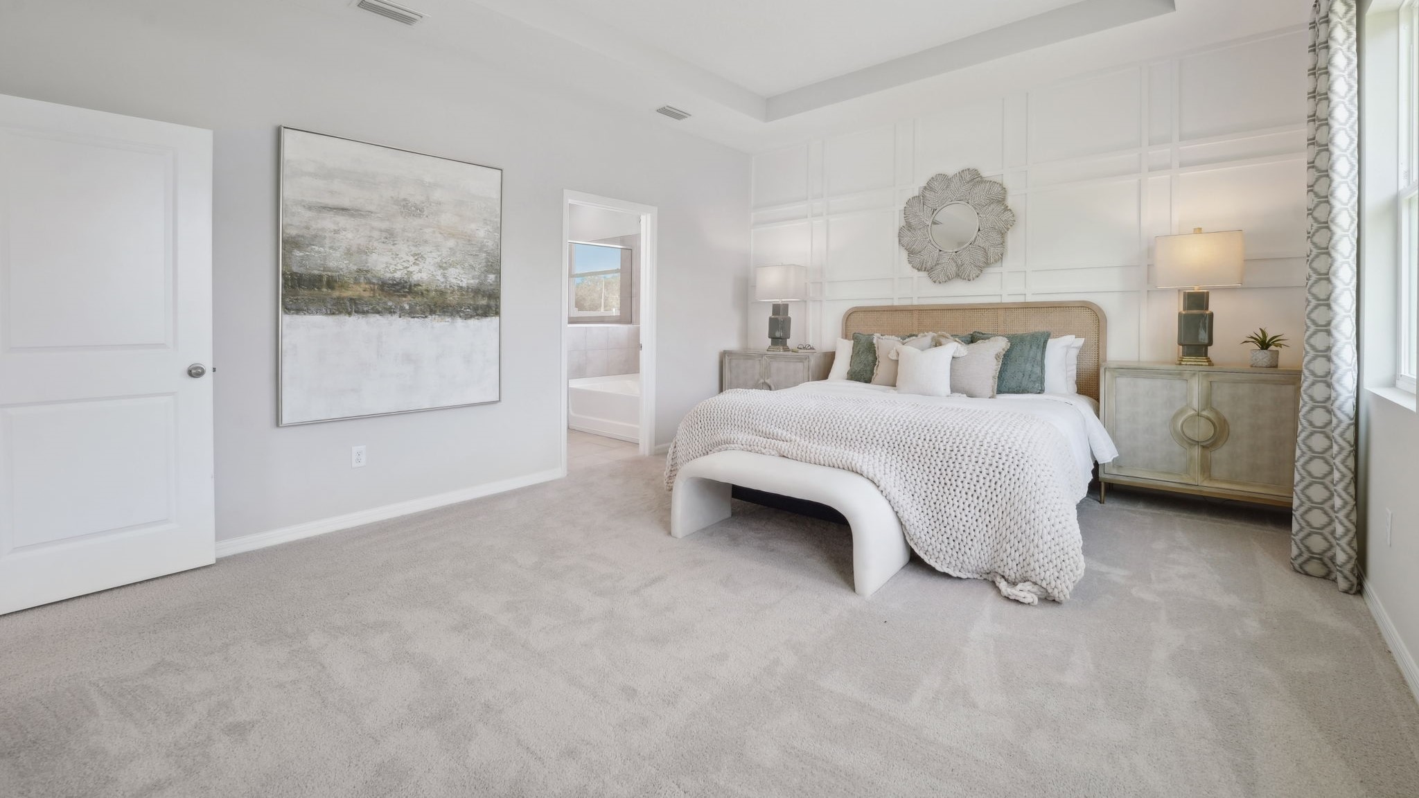 Spacious primary bedroom with king size bed, carpet flooring, natural lighting and a walk-in closet.