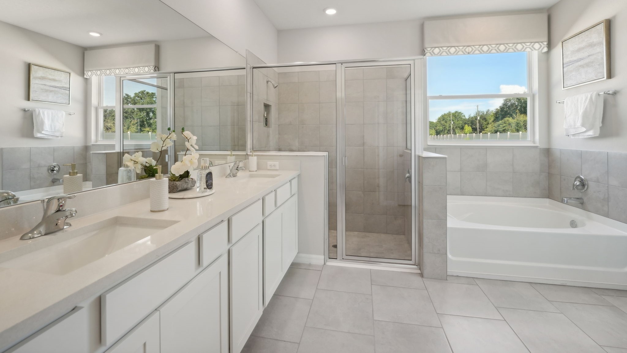 Modern bathroom with double vanity, large wall mirror, cabinets and quartz countertops along with walk-in shower.