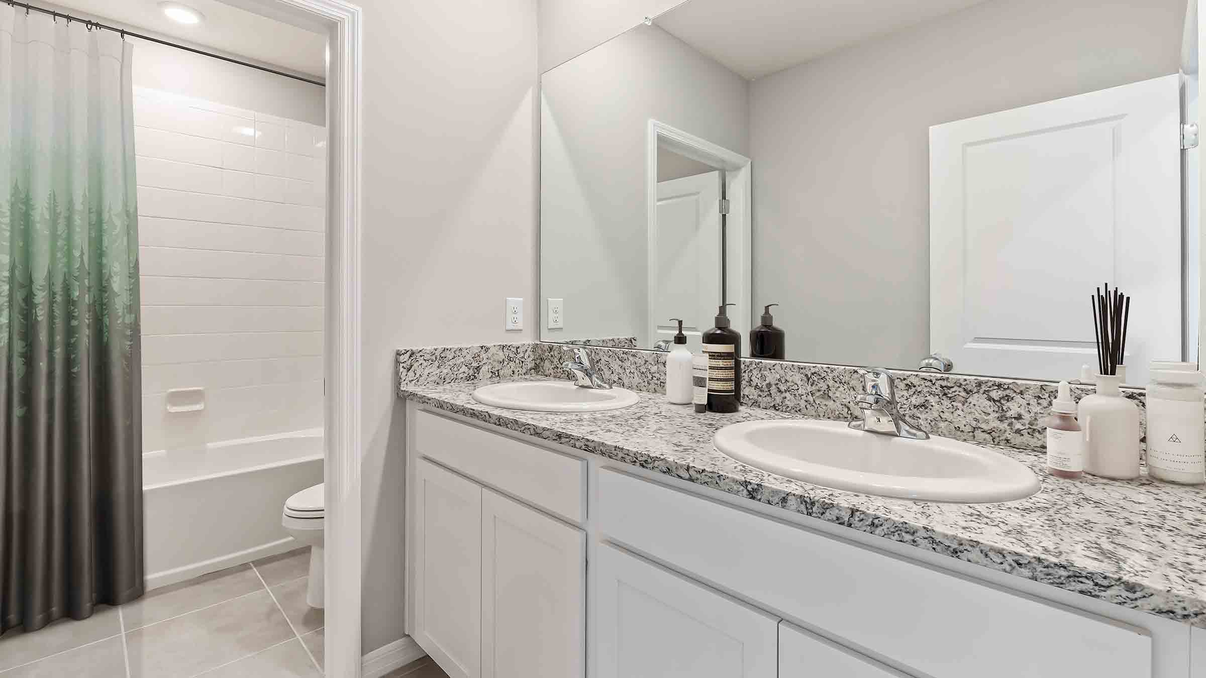 Modern bathroom with single bowl sink, quartz vanity, wall mirror, cabinets and toilet.