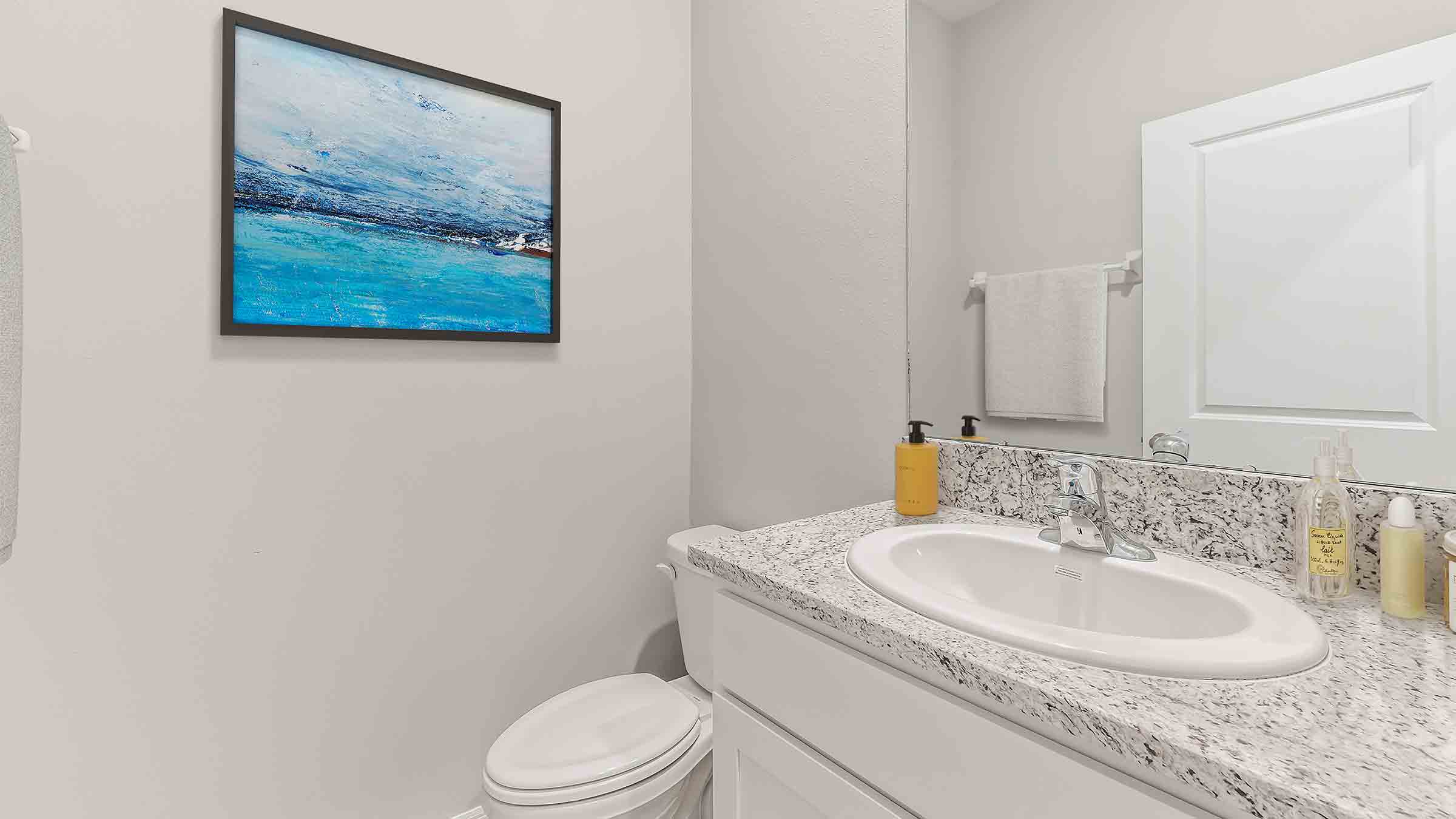 Modern bathroom with single bowl sink, quartz vanity, wall mirror, cabinets and toilet.