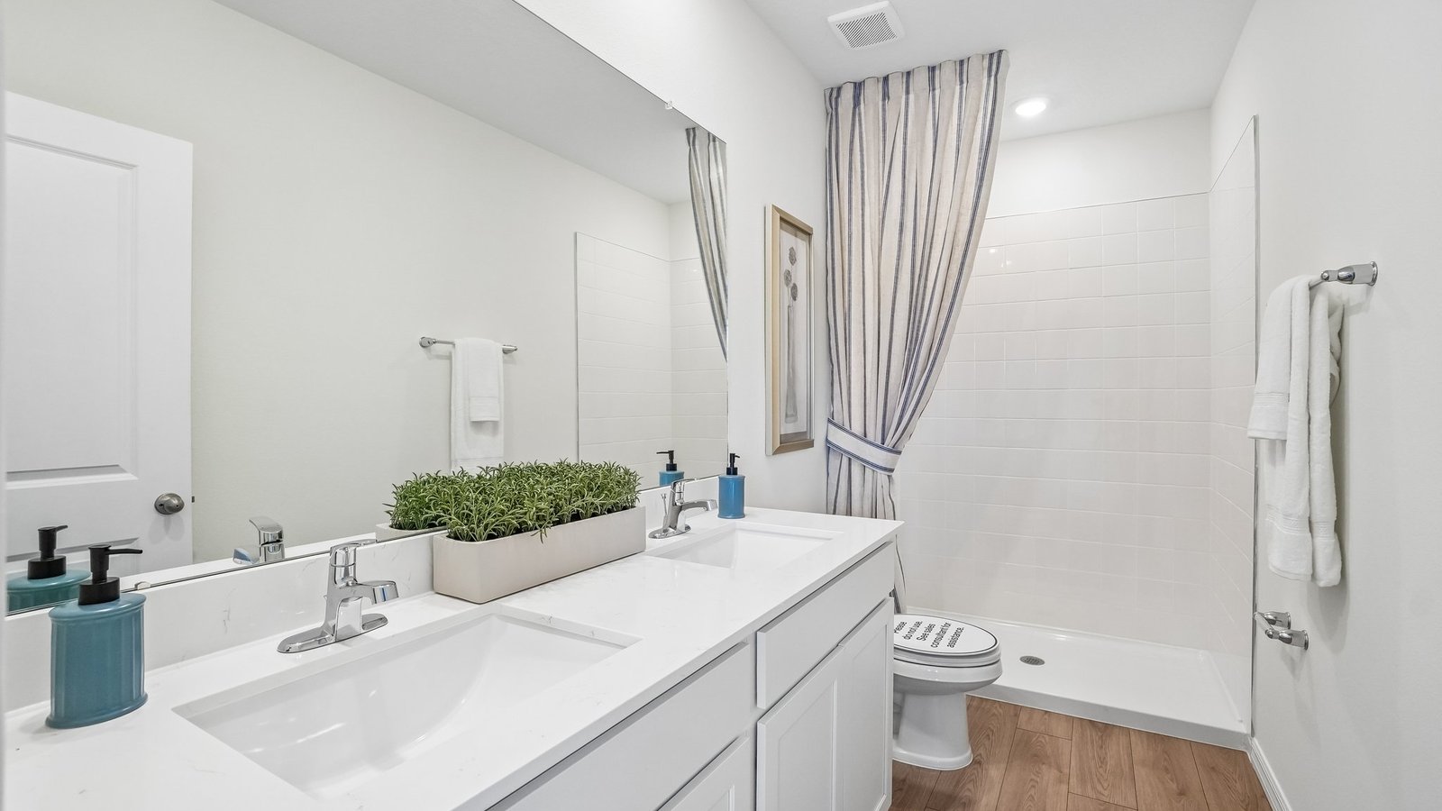 Modern bathroom with double vanity sinks, large wall mirror, cabinets and quartz countertops.