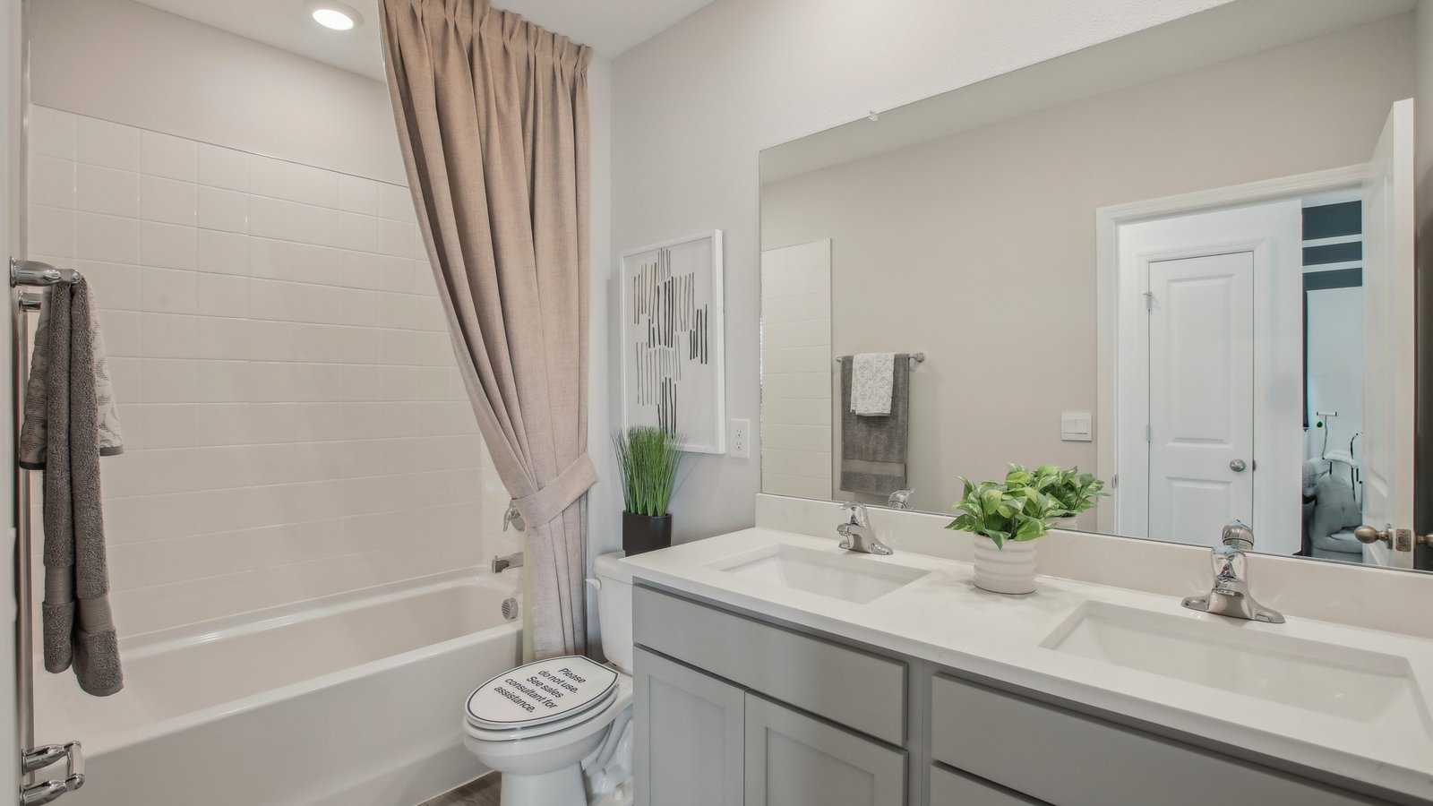 Modern bathroom with double vanity sinks, large wall mirror, cabinets and quartz countertops.