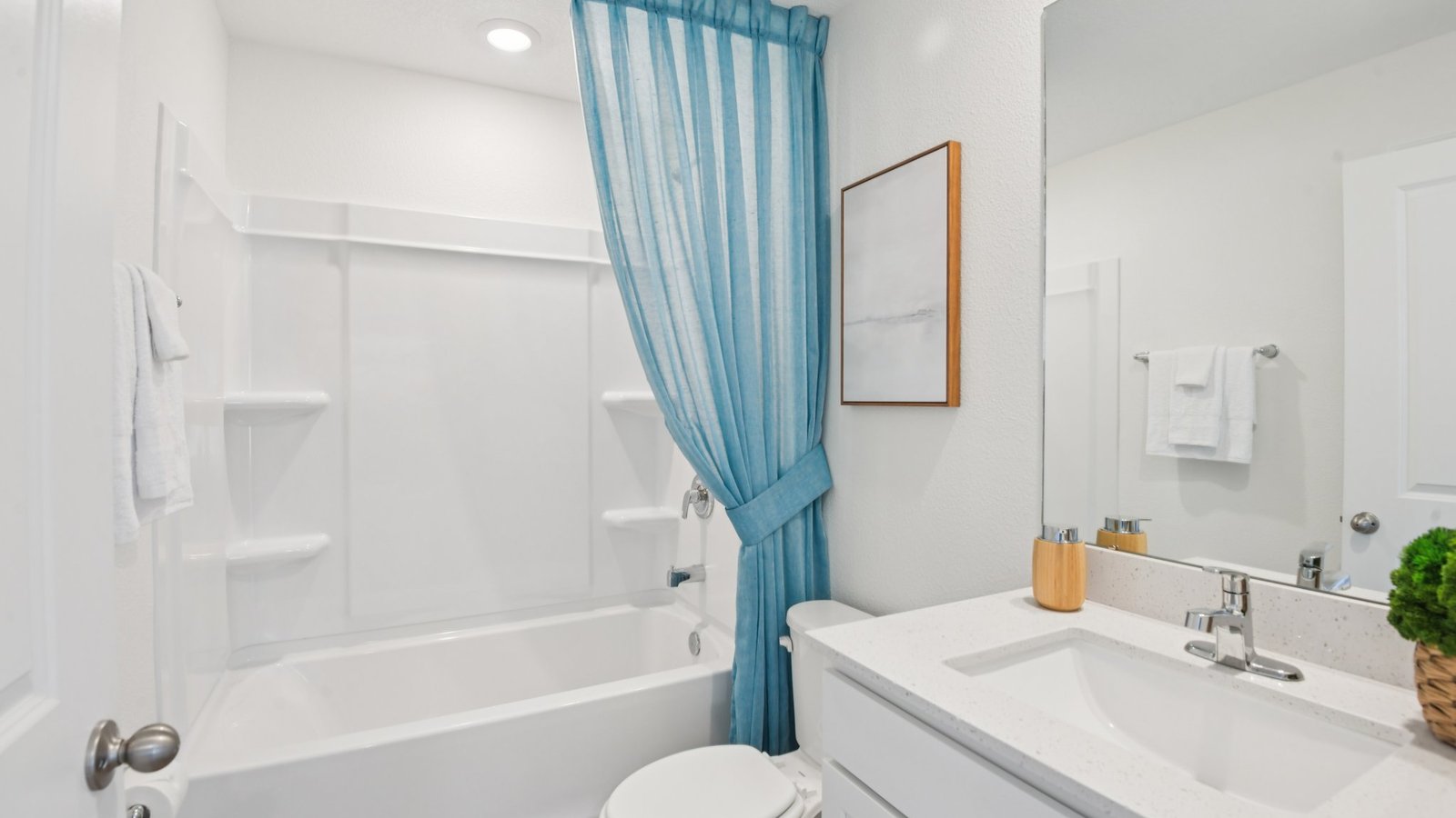 Modern bathroom with single bowl sink, quartz vanity, wall mirror, cabinets and toilet.