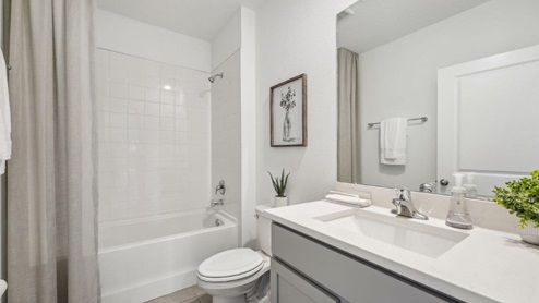 Modern bathroom with single bowl sink, quartz vanity, wall mirror, cabinets and toilet.