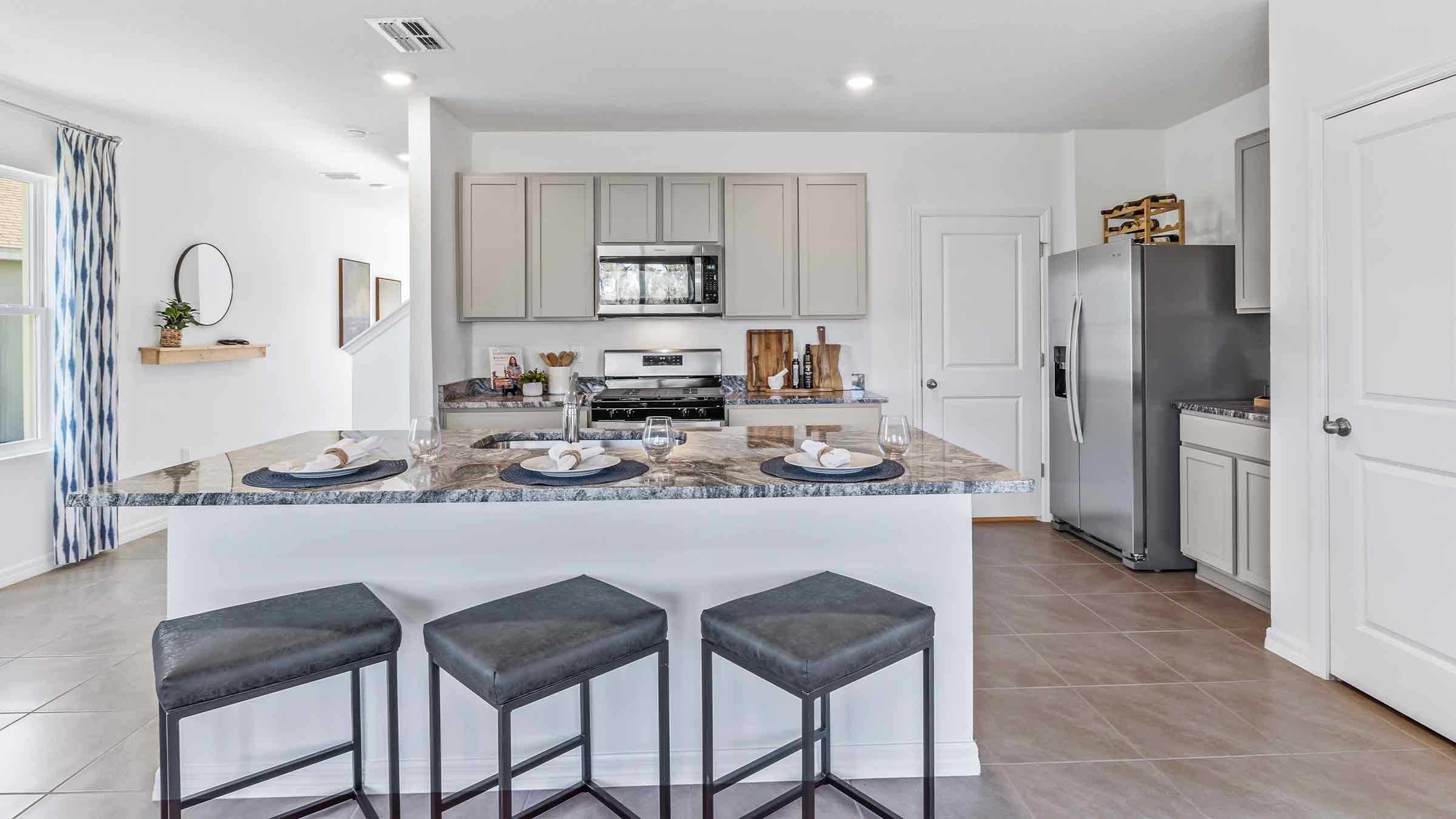 Kitchen with island seating, quartz counters, spacious pantry and stainless-steel appliances.