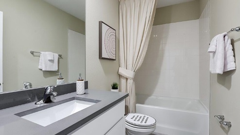 Modern bathroom with single bowl sink, quartz vanity, wall mirror, cabinets and toilet.