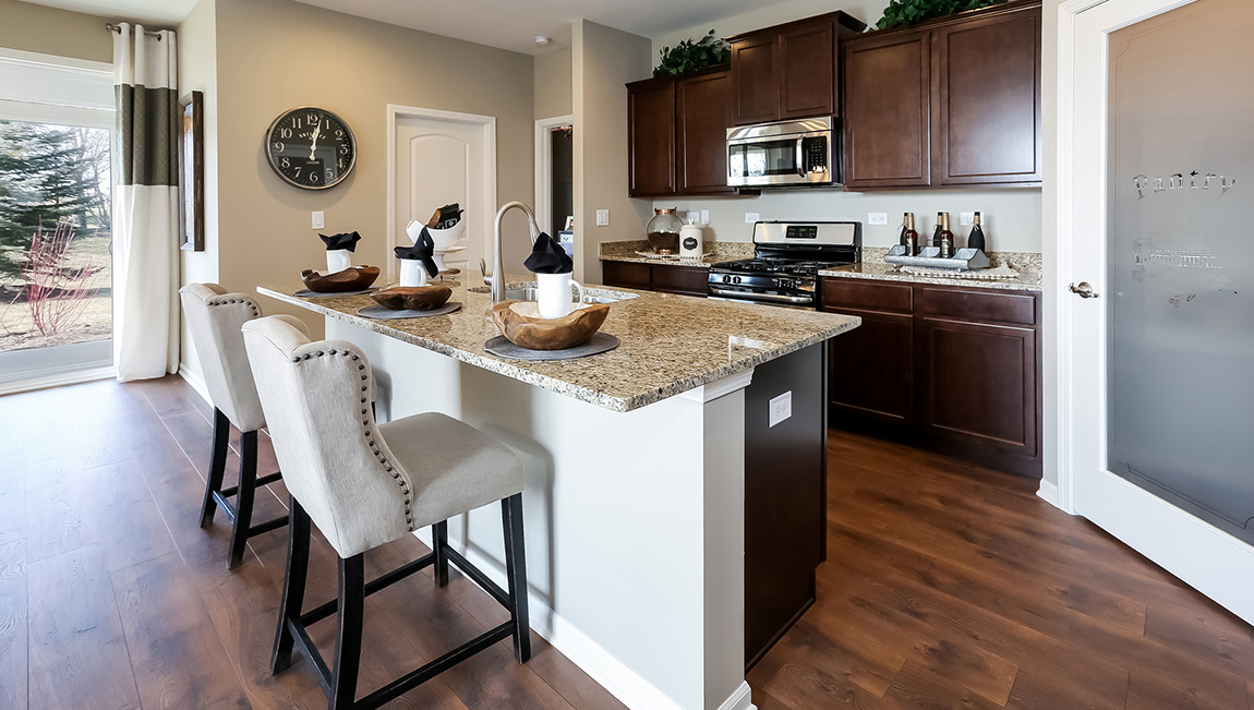 The spacious kitchen showcases an abundance of dark wood cabinetry with large island with stainless steel appliances. Pantry to the left.