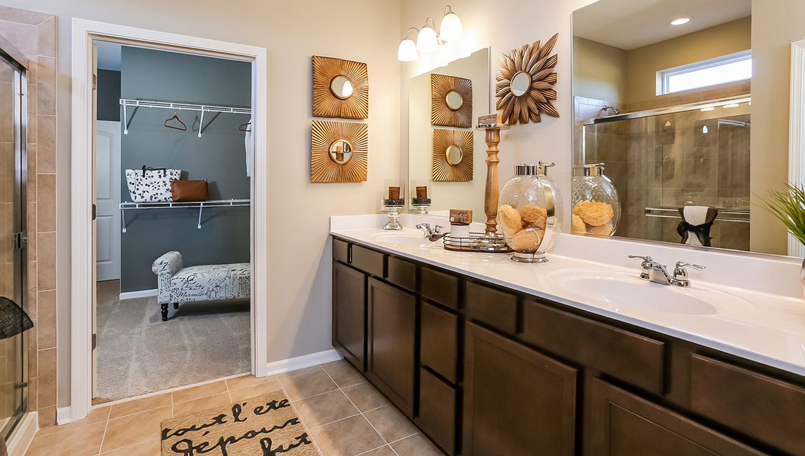 Connecting primary bathroom with dark wood colored 2 sink vanity and glass shower. Connecting closet to the bathroom.