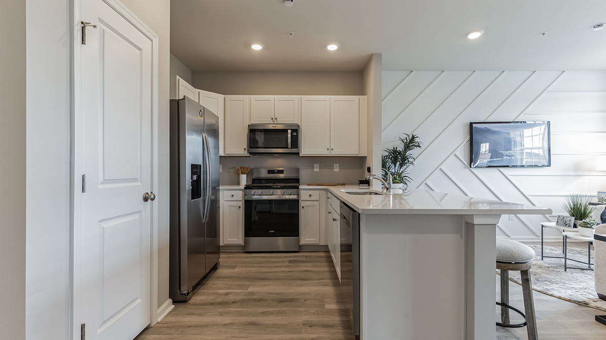 Directly looking into the kitchen with the fridge and pantry to the left, stove in the back, and the counter or island to the right with a peek into the living area.