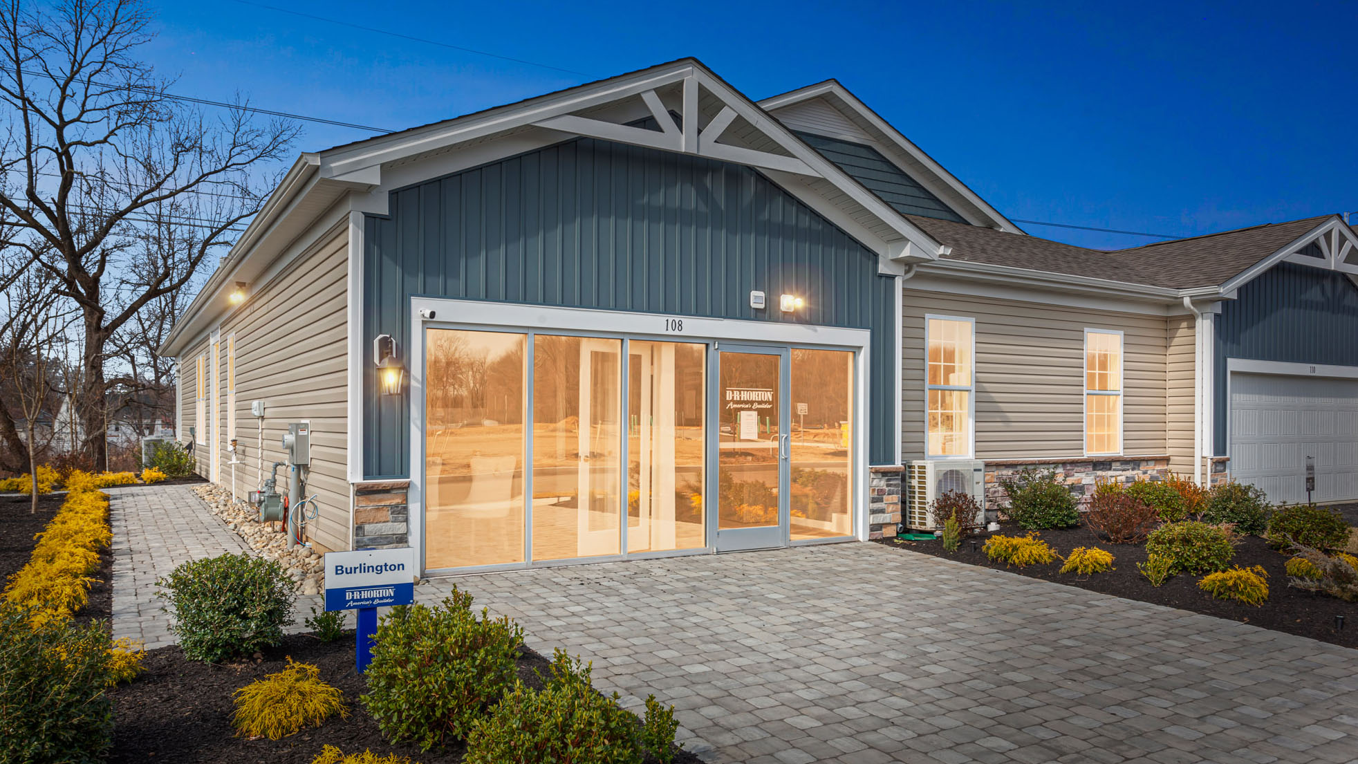 A dusky image of Silver Lake Reserve Burlington plan single-story twin home in wicker color siding, midnight surf board and batten accent siding, and white garage door.