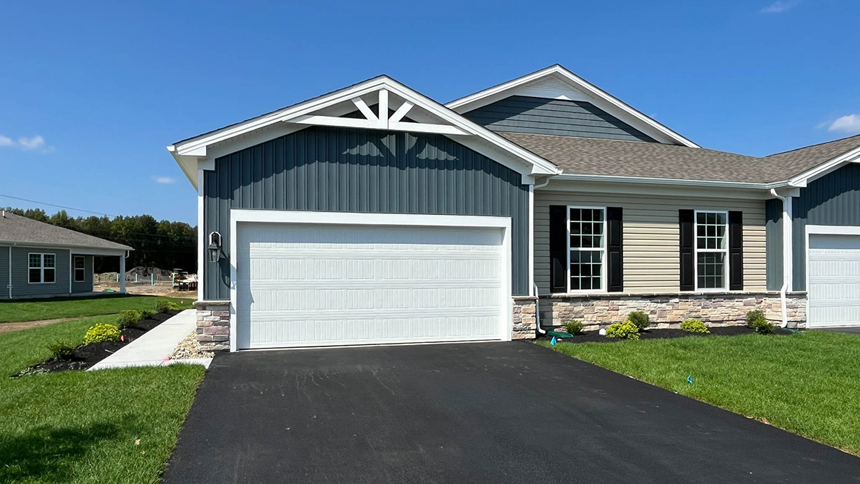 Burlington plan single-story twin home in wicker color siding, midnight surf board and batten accent siding, black shutters, and white garage door.
