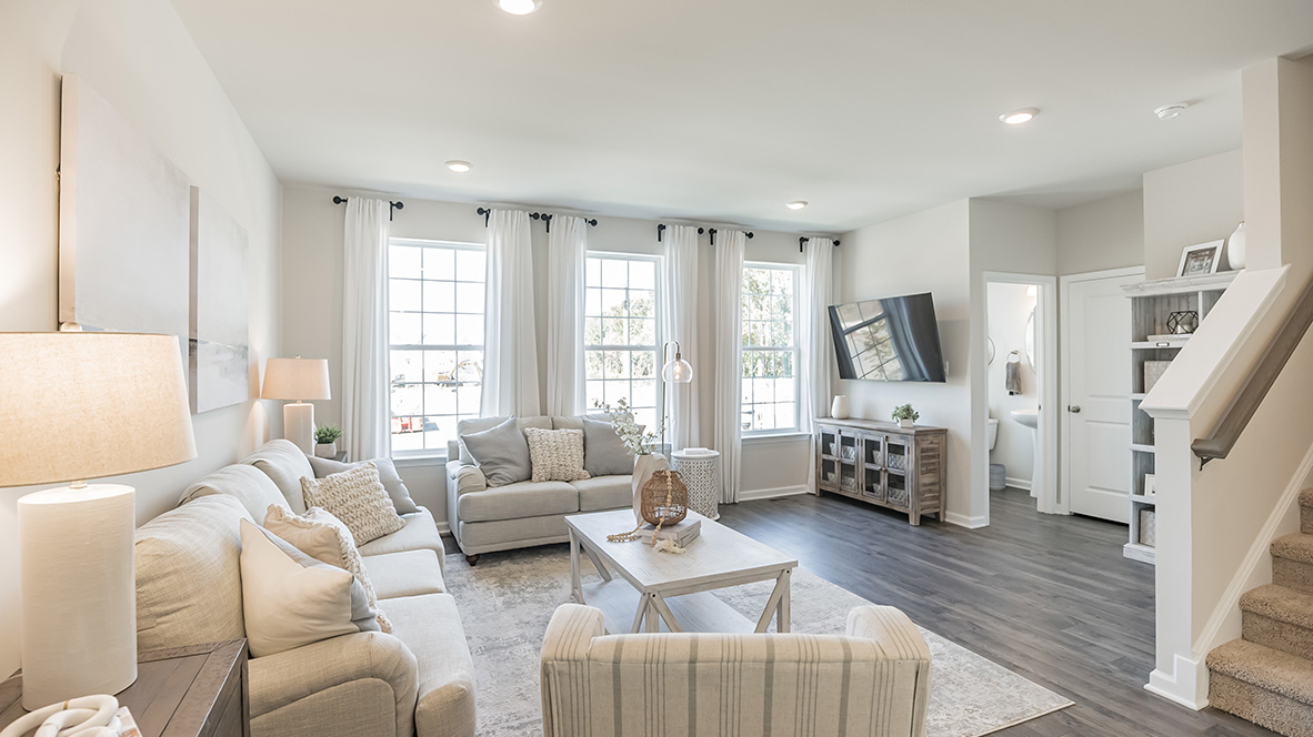 Living area with the stairs to the right and the half bath in the back right with windows coving the entire back wall.