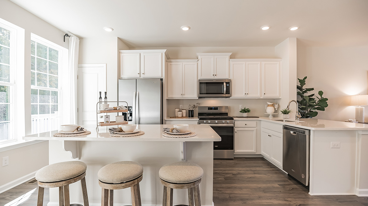 Bright spacious kitchen area with large island with white counter tops and white cabinetry and stainless steel appliances.