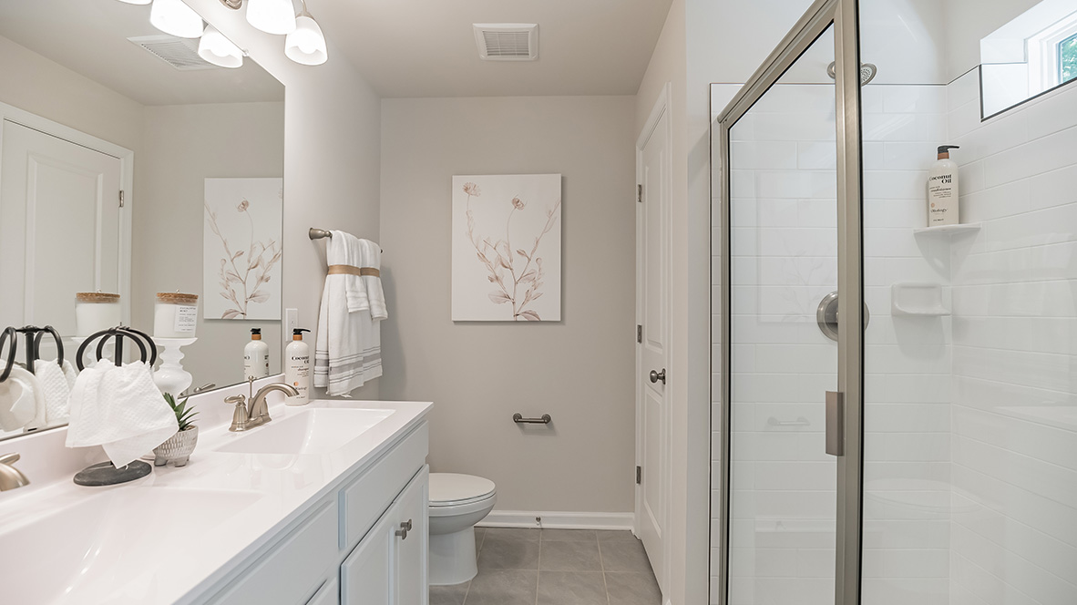 Primary bathroom with double sink white vanity with glass door shower and linen closet.