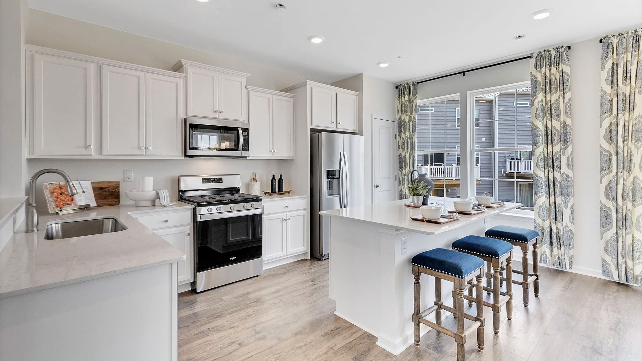 Bright spacious kitchen area with large island with white counter tops and white cabinetry and stainless steel appliances.