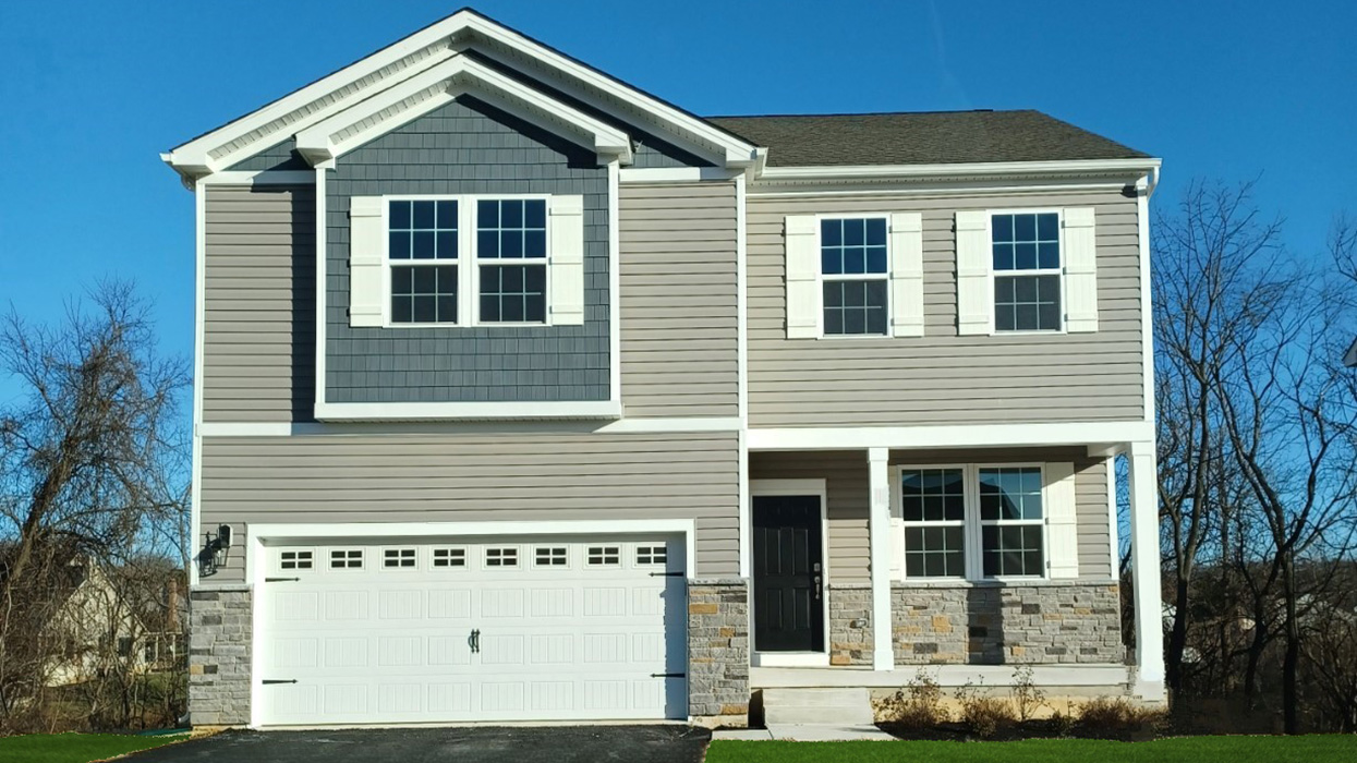 A two-story Penny home with gray siding and navy shake accent siding, stone kneewall, and a white two car garage.