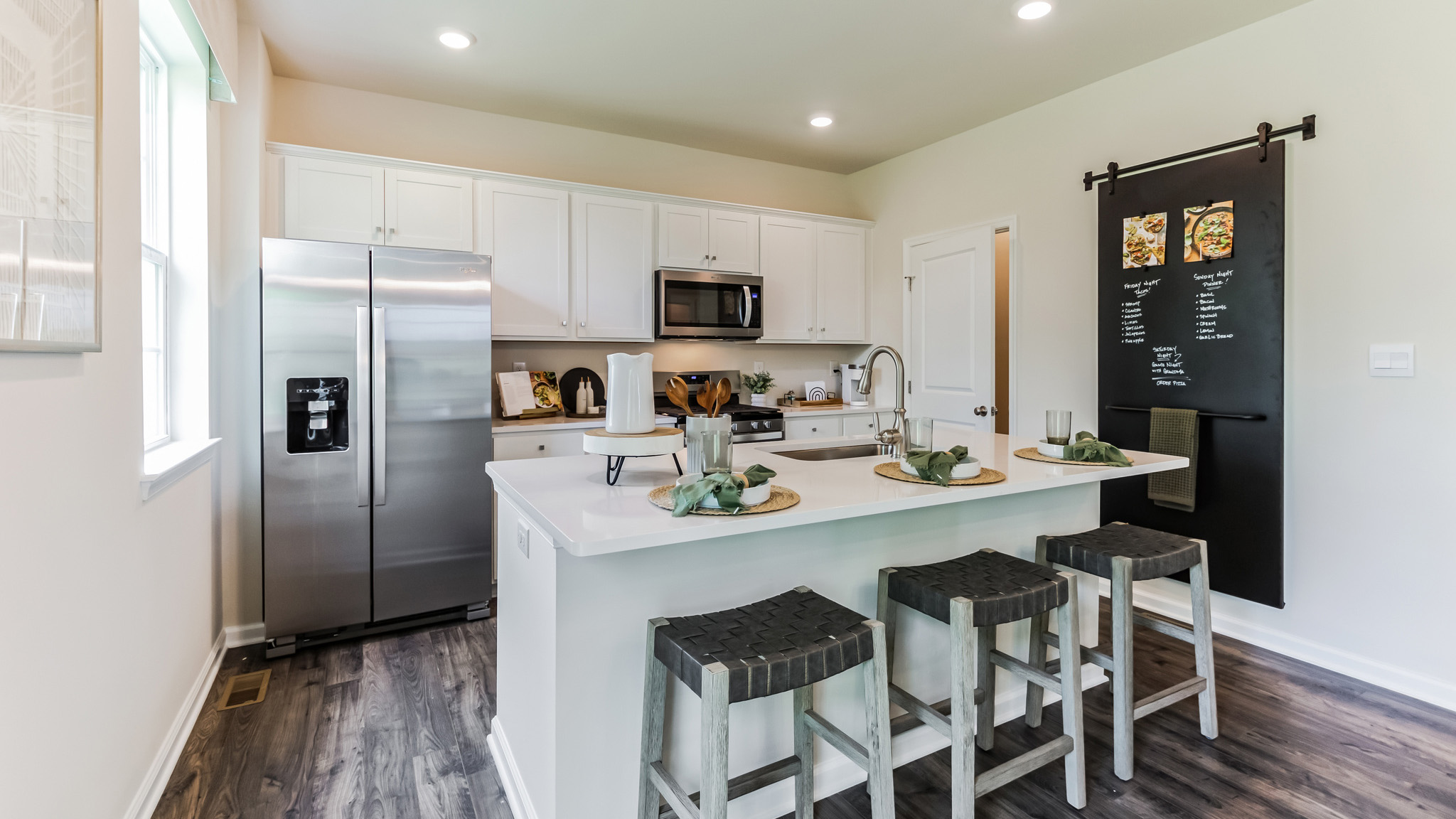 Wide view of the kitchen with island seating and stainless steel appliances.